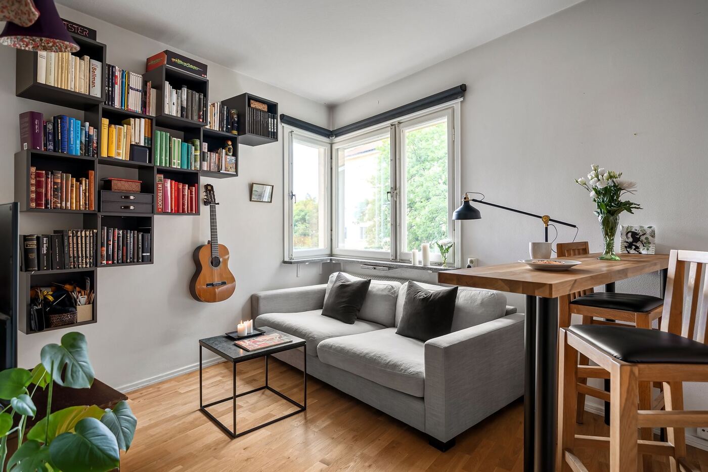 Salón luminoso con estanterías de libros, sofá gris y ventanas en esquina
