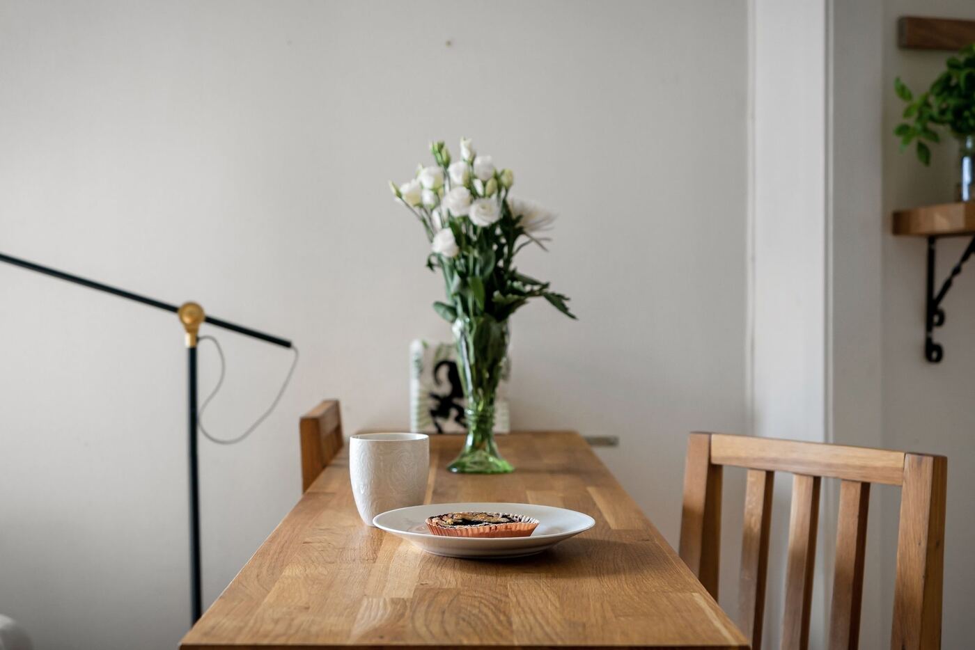 Mesa de madera con flores blancas junto a una lámpara de pie